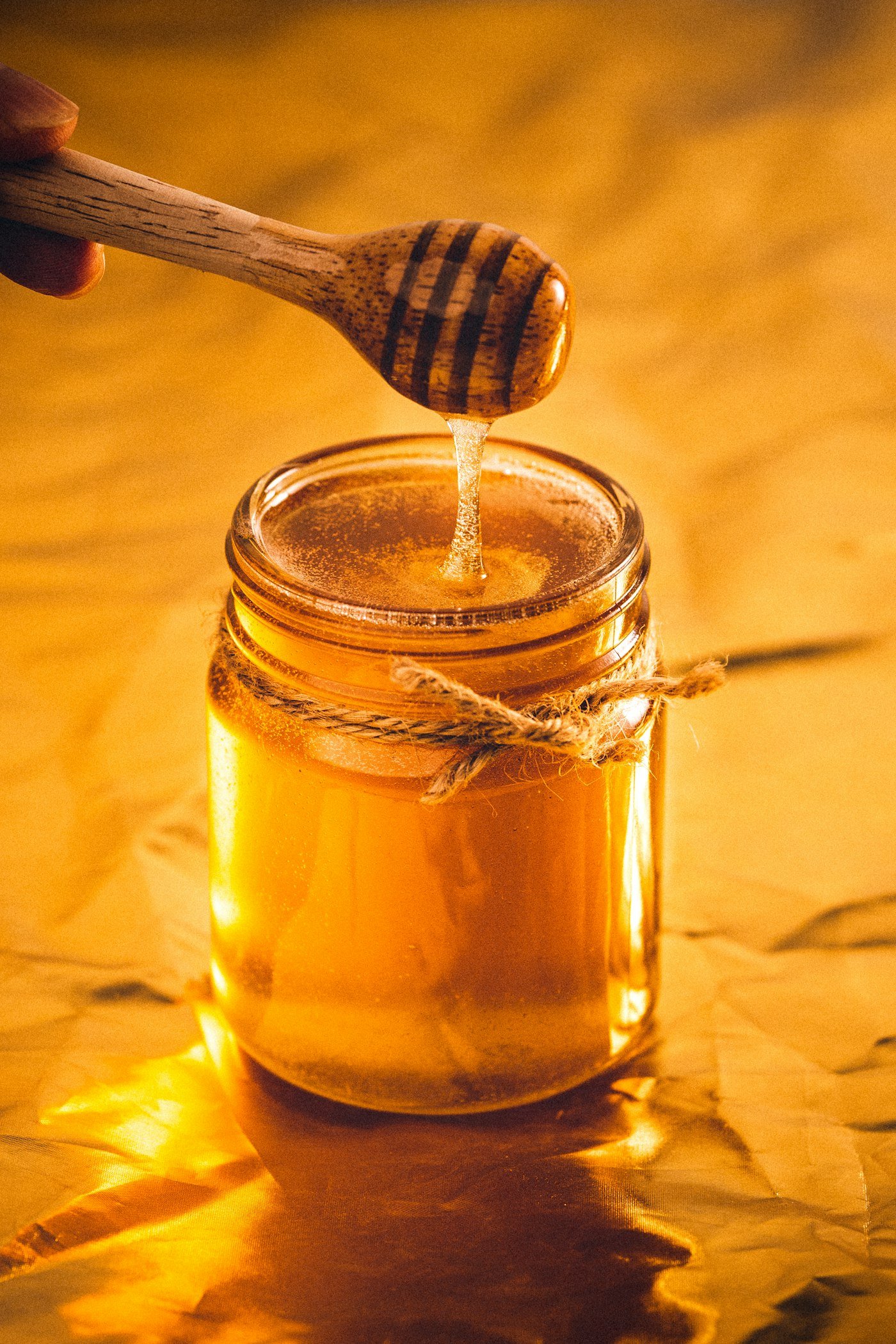 Golden raw honey in a glass jar with a wooden dipper