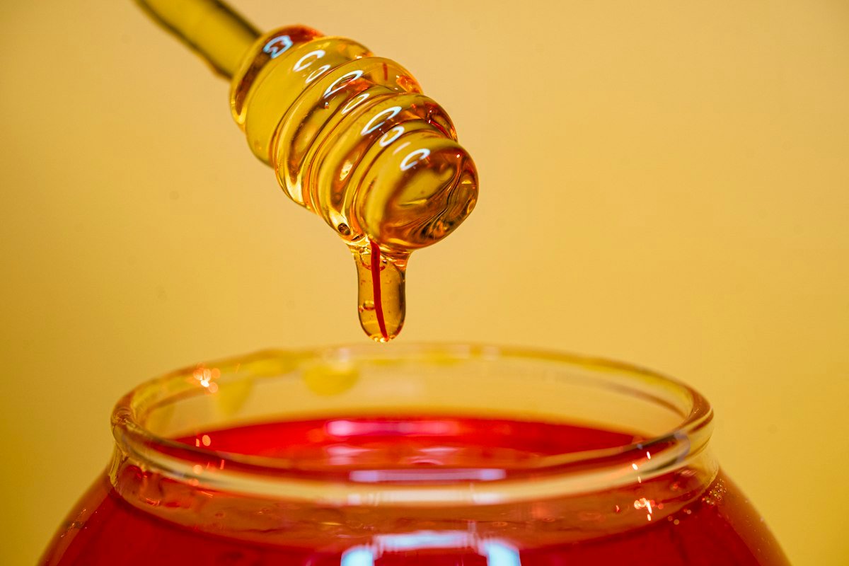 Honey dripping from a dipper into a jar